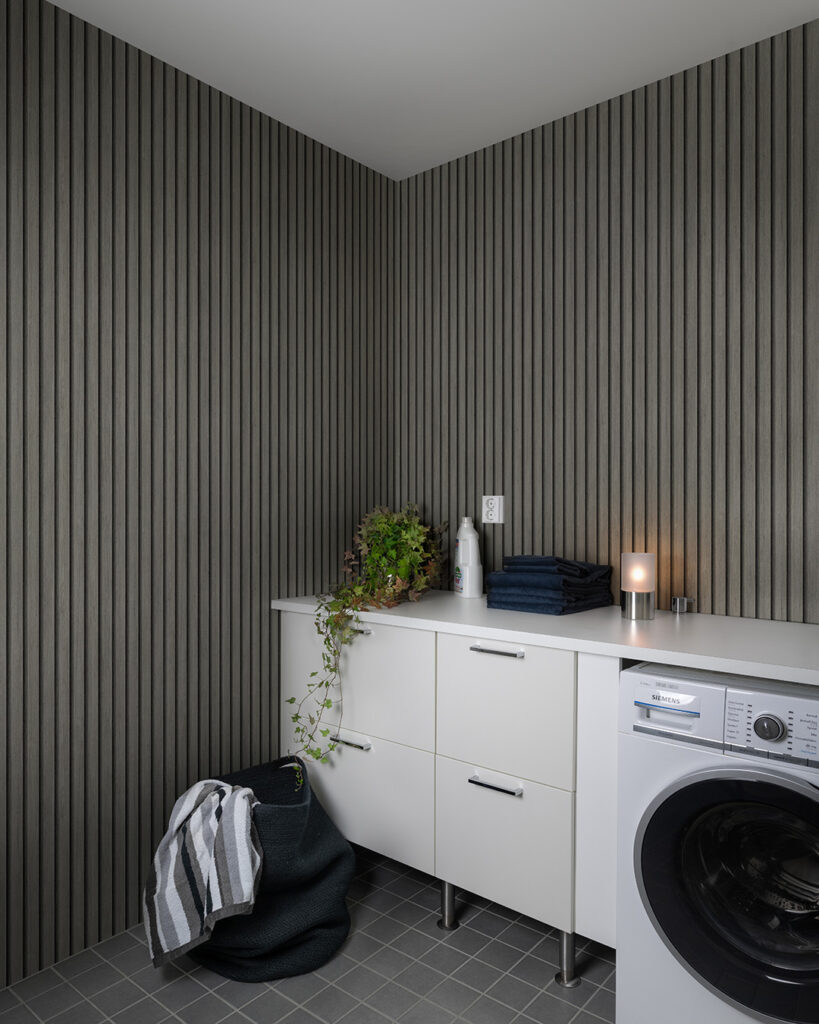 wood-panel wallpaper in a laundry room behind a white bench with a plant and a lamp on it