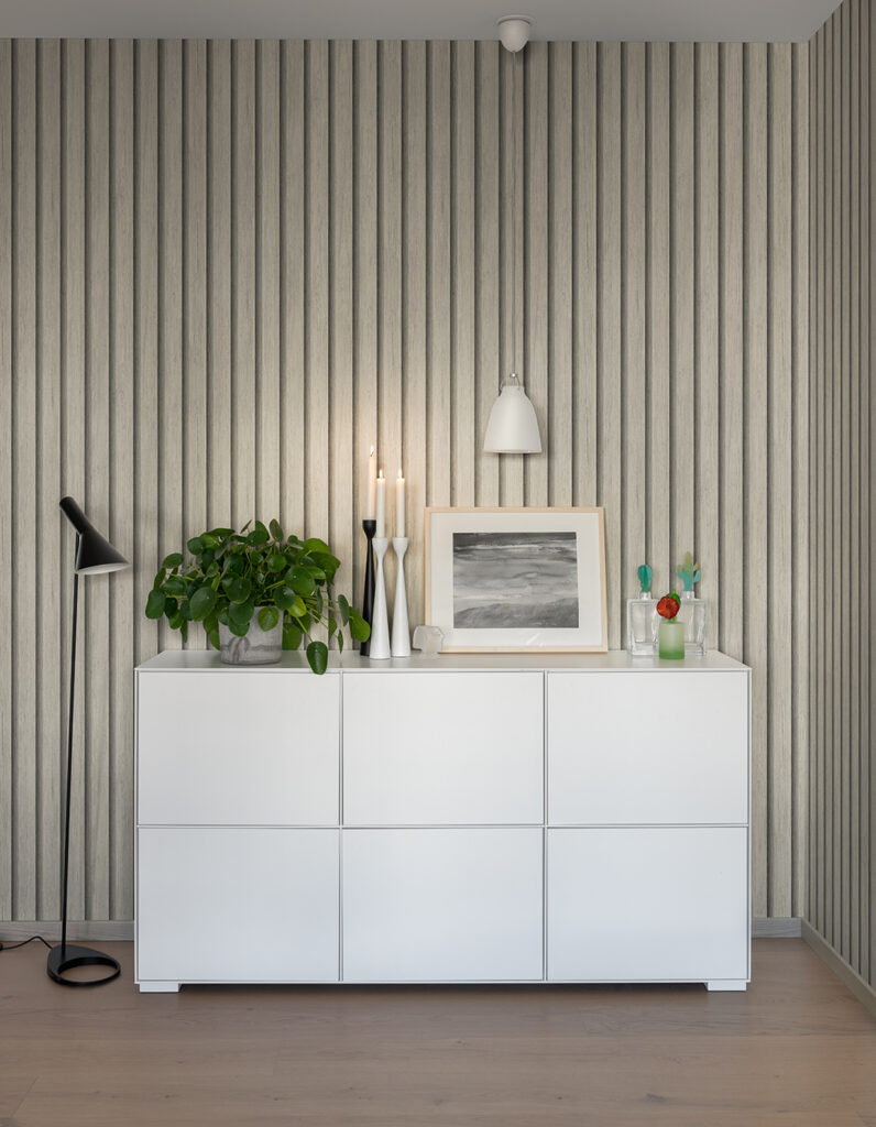Ljus träpanels tapet i en hall bakom en vit byrå med blommor och ljus på