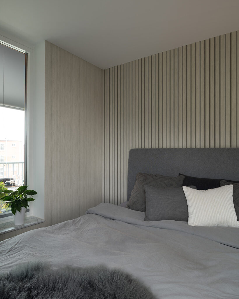 Light-colored wood-panel wallpaper behind a large gray bed in a bedroom