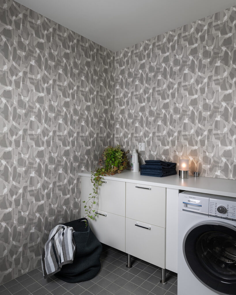 Gray geometric camouflage wallpaper in a laundry room behind a white bench