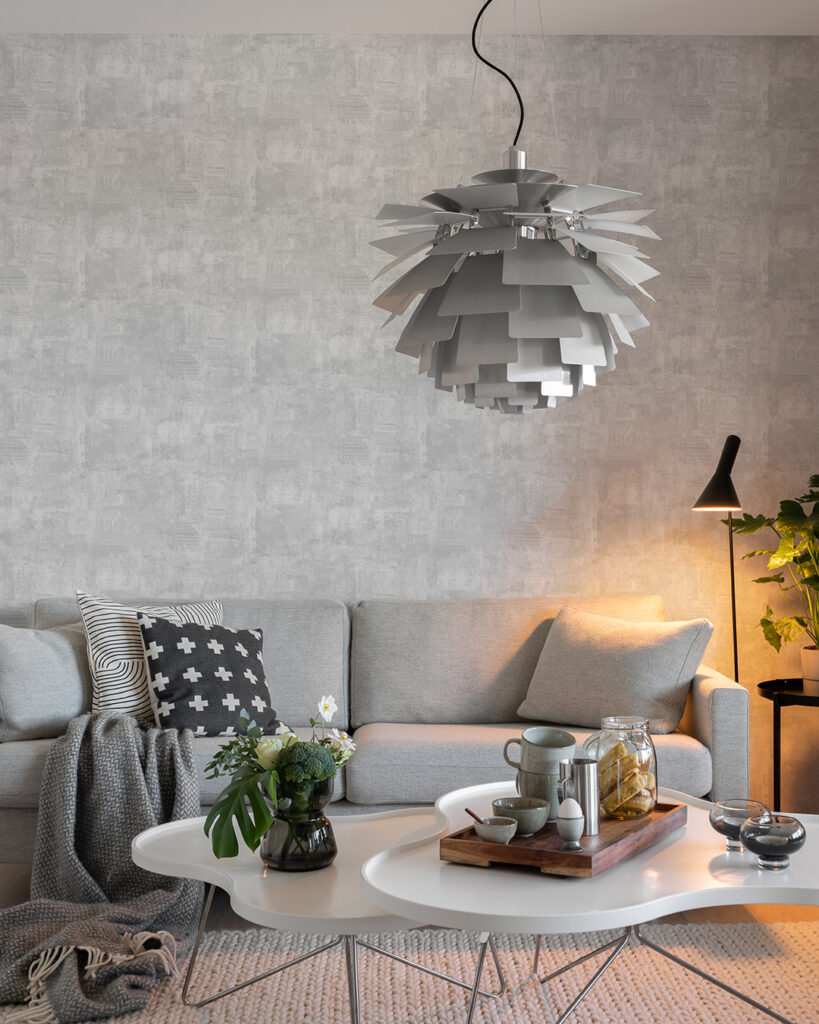 Ljusgrå cement tapet i ett vardagsrum bakom en grå soffa och en stor geometrisk lampa