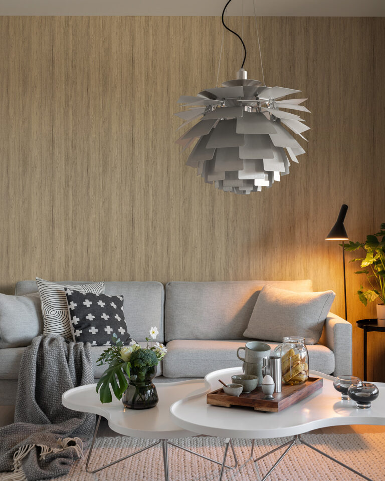 Wood-paneled wall in white-oiled oak in a living room behind a gray sofa and a large chandelier