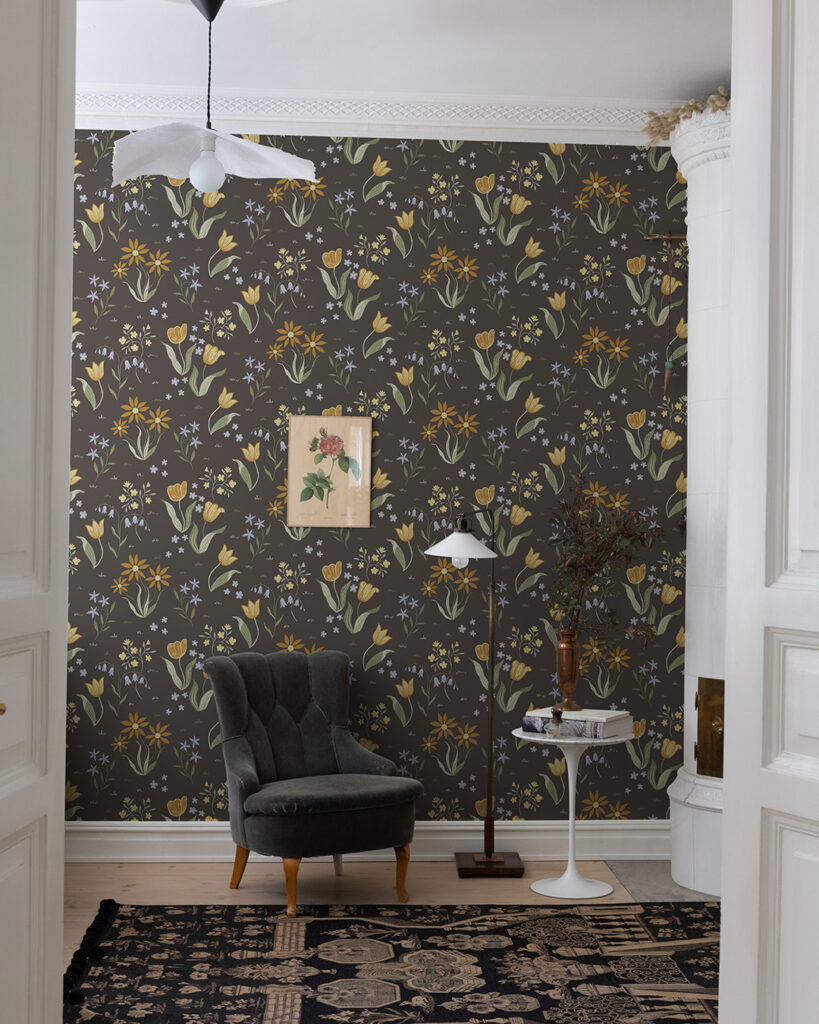 Dark wallpaper with flowers in orange, yellow, green, and blue in a living room with a black armchair and a large patterned rug