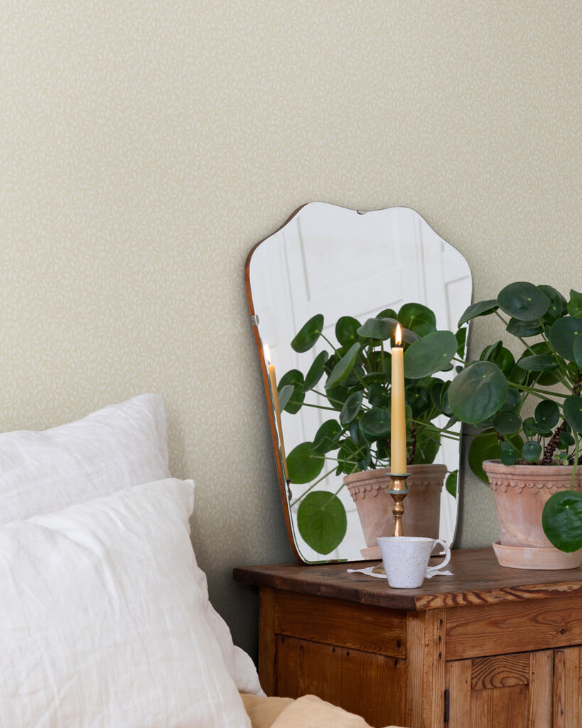 Beige tapet med ljusare små blad i ett sovrum bakom en spegel och en grön krukväxt