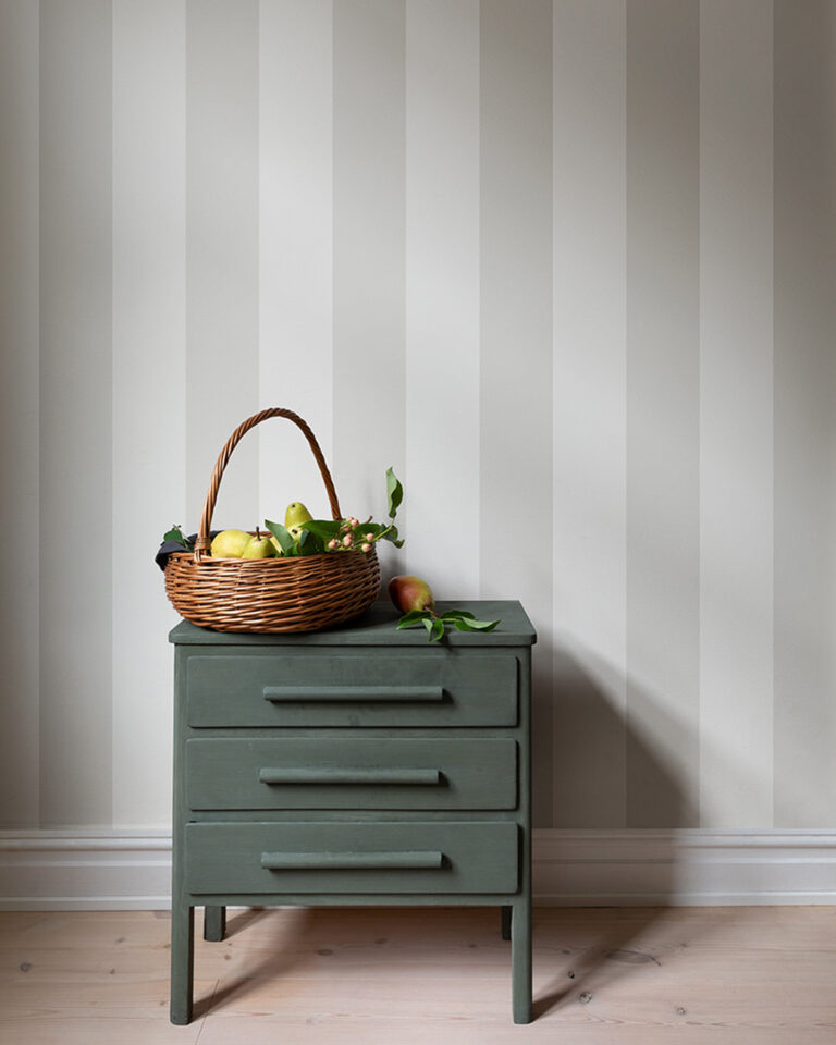 Light-colored striped wallpaper in a hallway with a green dresser and a basket of fruit on it