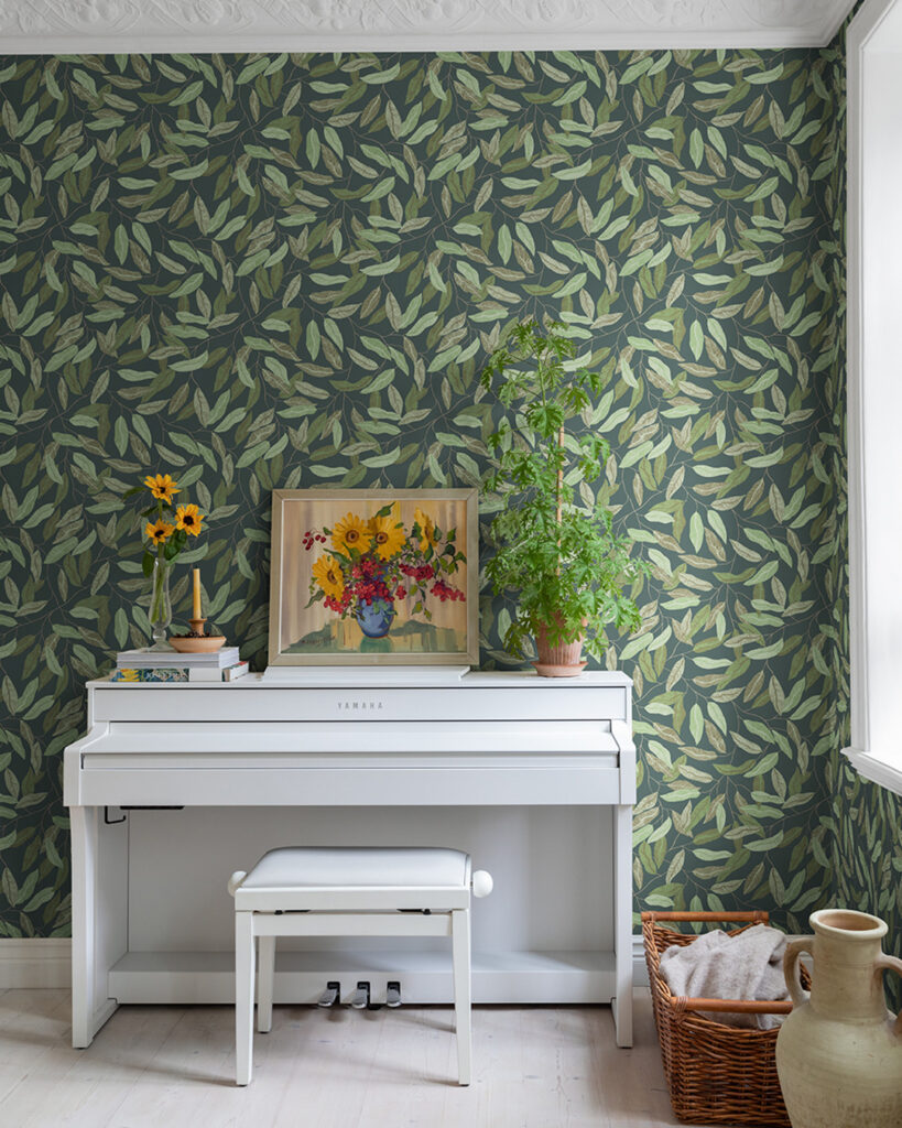 Gråtapet med gröna blad bakom ett vitt piano