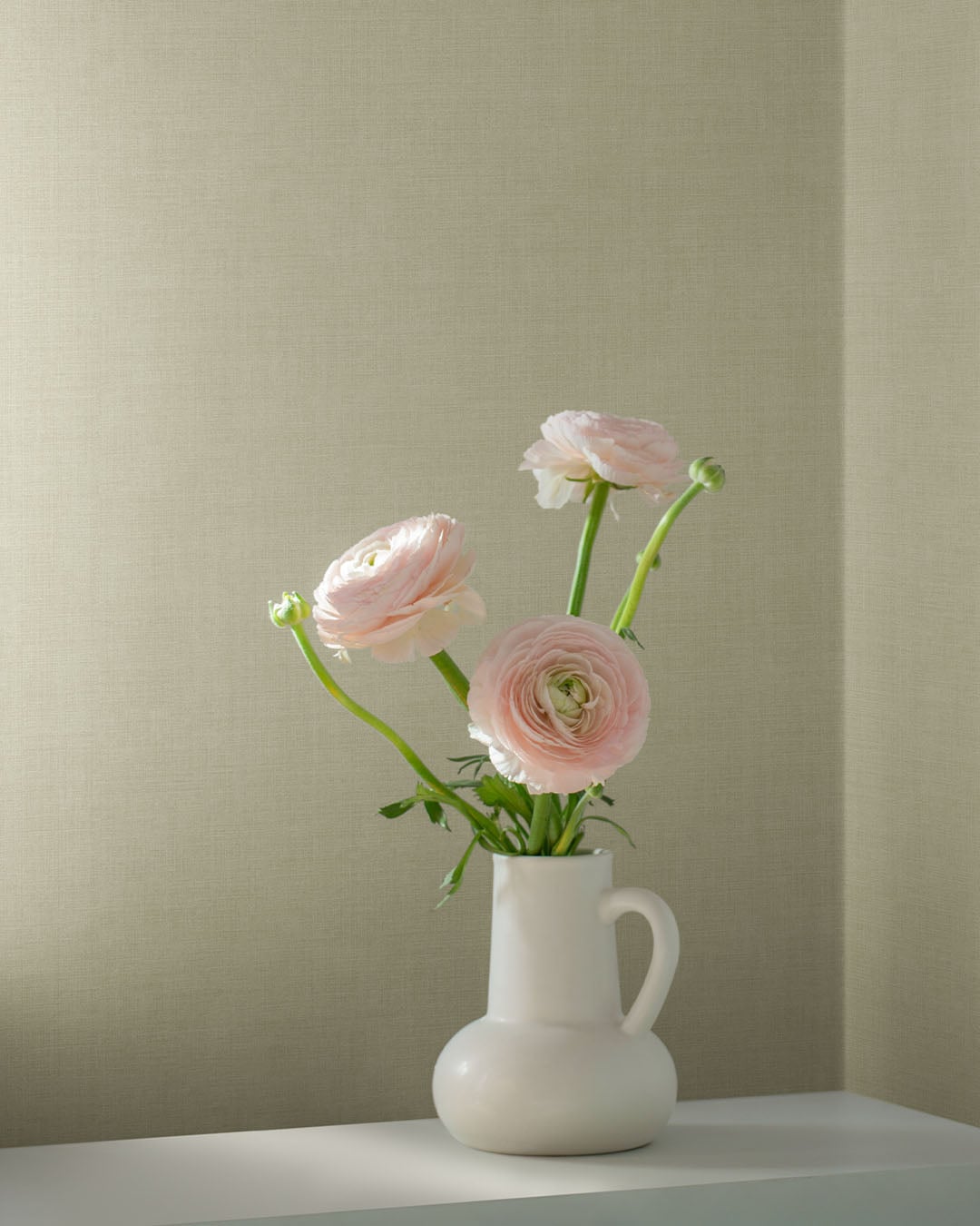 Beige linen wallpaper creates a cozy atmosphere, complemented by a bouquet of pink flowers on the table.