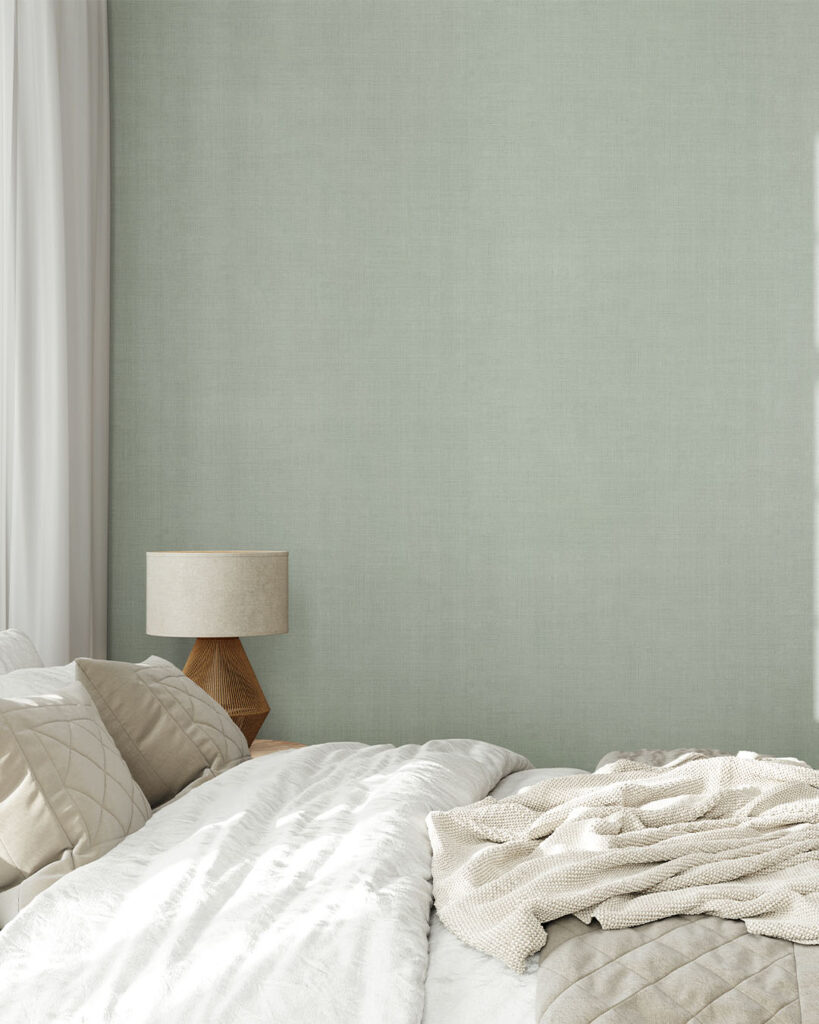 A light gray-green solid-color linen wallpaper whose textile texture creates a sense of calm in a bedroom with light-colored textiles.