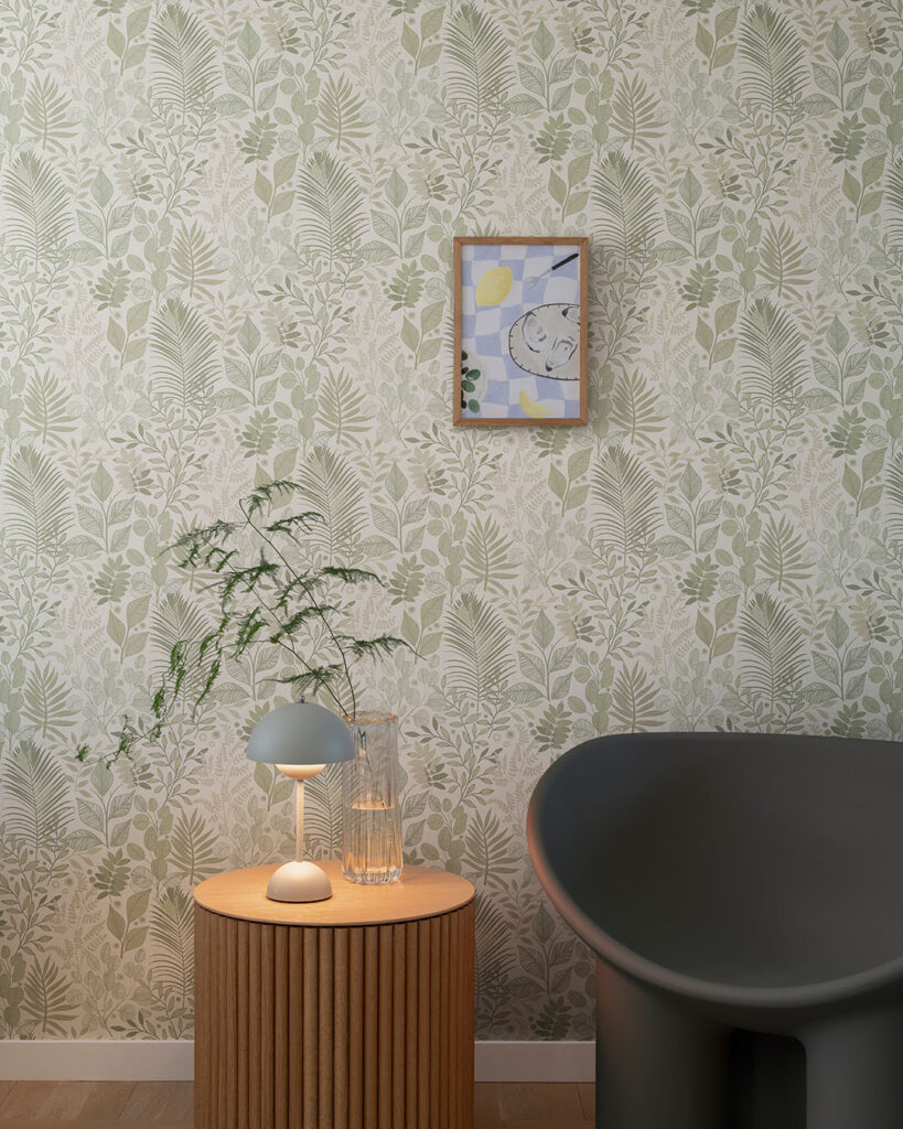 White wallpaper with green leaves in a living room with a black armchair