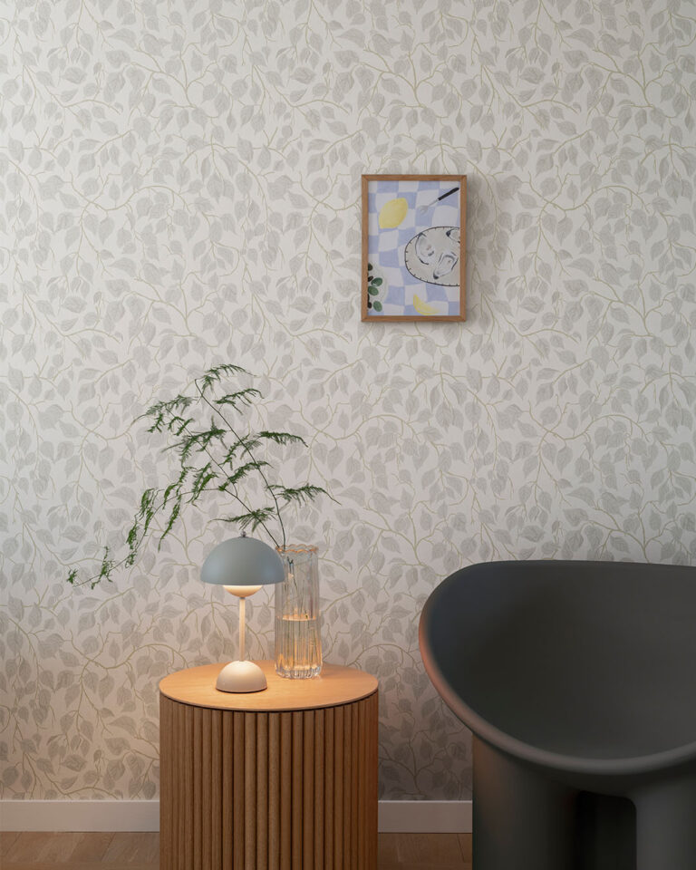 White wallpaper with winding leaves in a living room with a black armchair