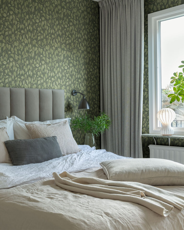 Green wallpaper with curving leaves in a bedroom with a made bed