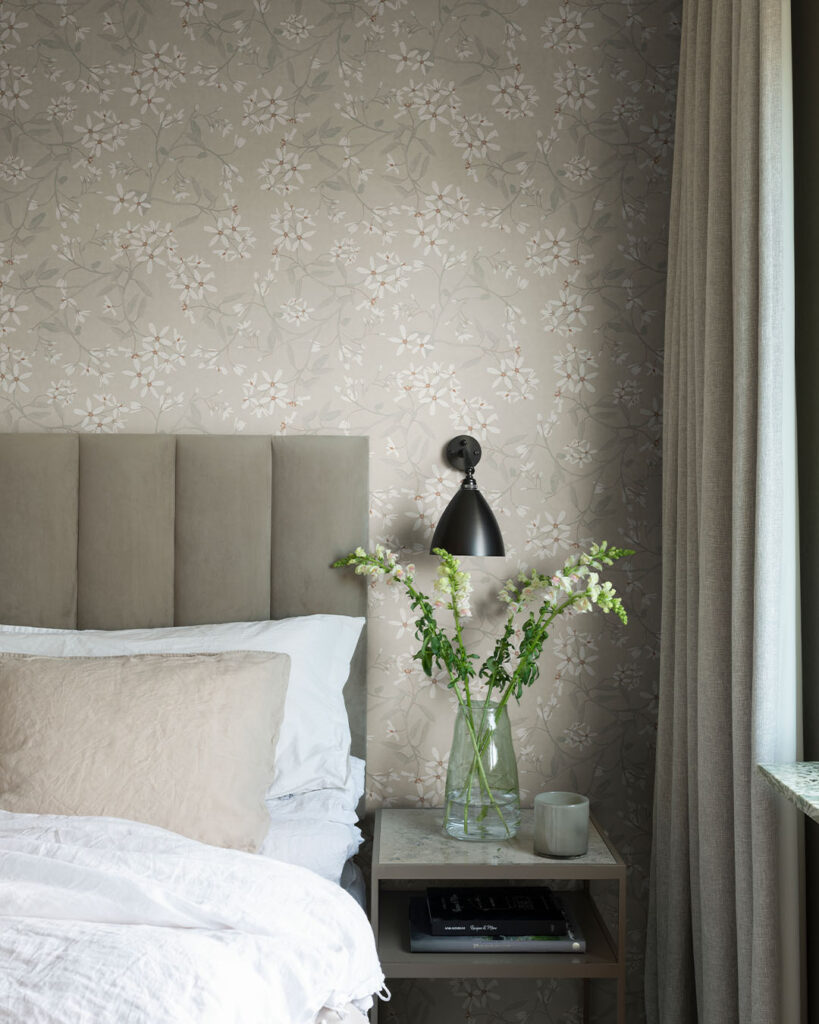 Tapet med tunna blommor i vitt med beige botten i ett sovrum med en bäddad säng