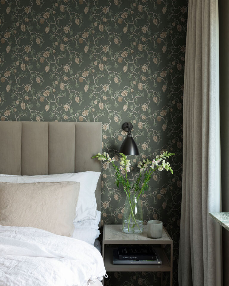 A cozy bedroom with dark wallpaper featuring pine branches and pinecones