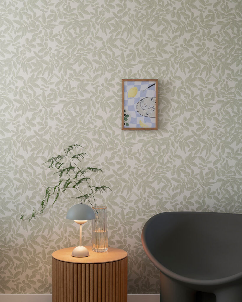Wallpaper with a green leaf pattern on a warm white background in a living room with a black armchair