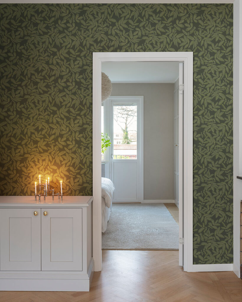 Wallpaper with a green leaf pattern on a dark green background in a hallway with a white dresser