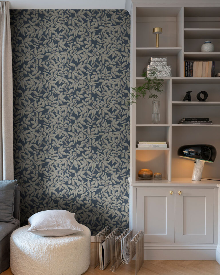 Wallpaper with a gray leaf pattern on a dark blue background in a living room with a white bookshelf