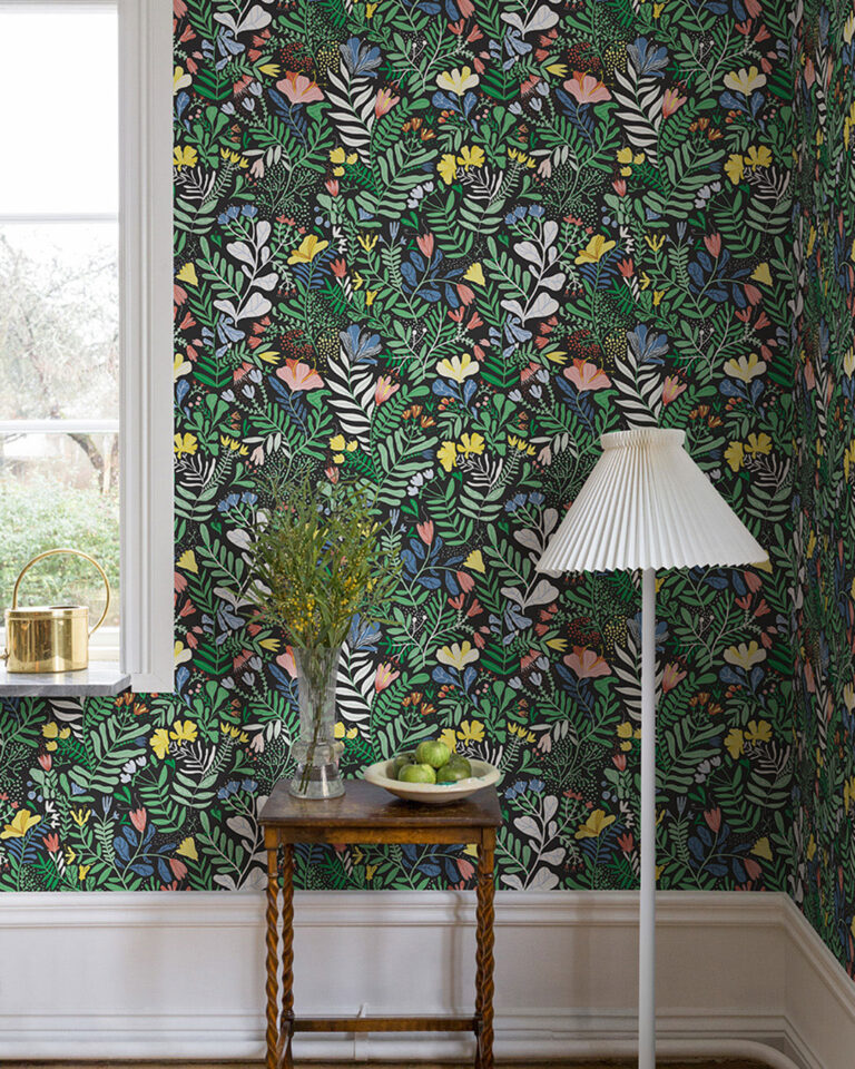 Svart tapet med färgglada blommor och blad i en hall bakom en vit golvlampa och ett litet träbord