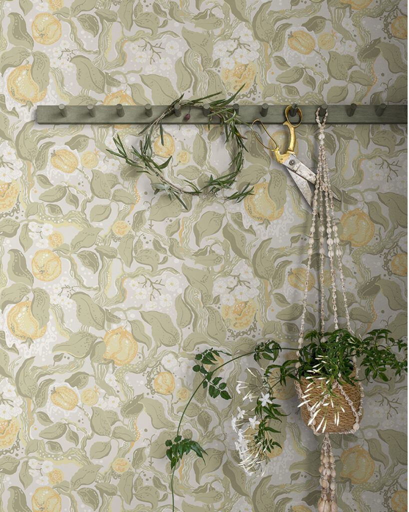 A green hook rack with a pot hanging in front of wallpaper featuring apples and leaves.