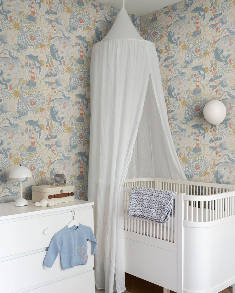Blue, colorful wallpaper with a seaside motif and suns in a child's room with a crib