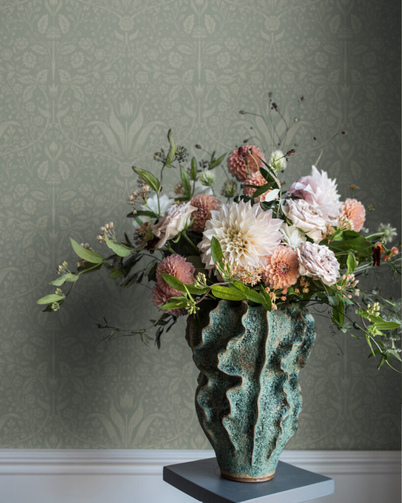 Ton i ton tapet sekelskifte stil med gröngrå botten och ljust gröna tulpaner bakom en grön vas med färgglada blommor