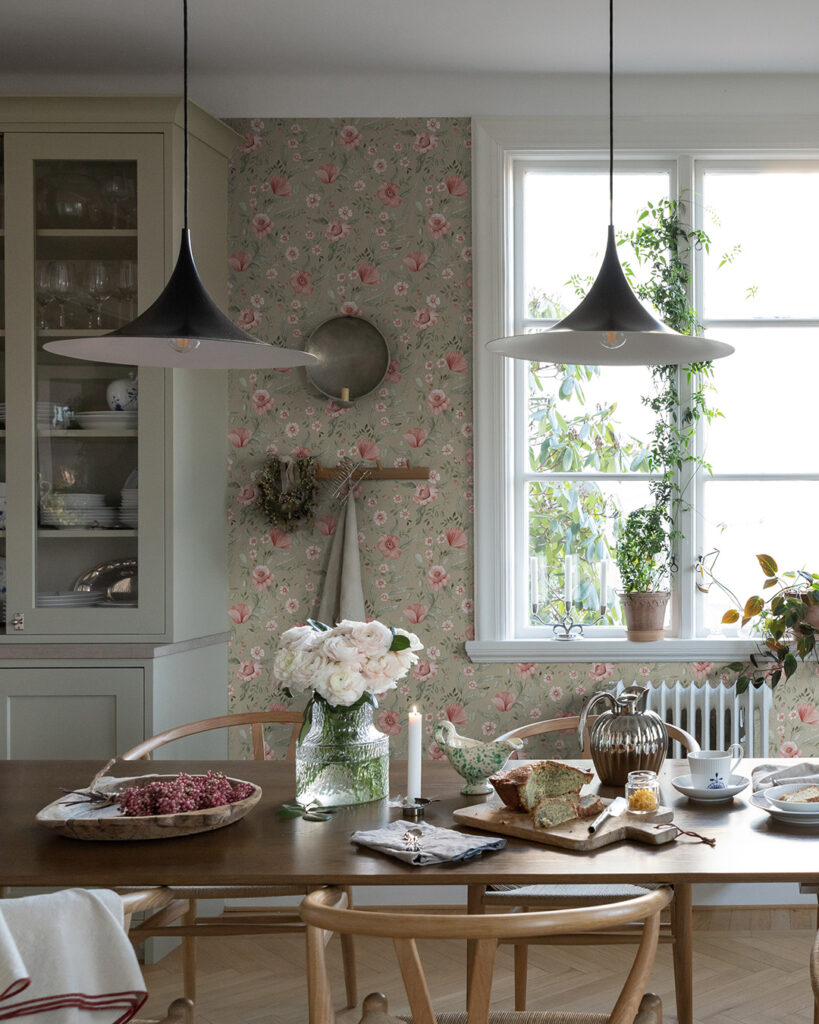 Tapet med rosa blommor i ett kök med träbord och ett stort fönster