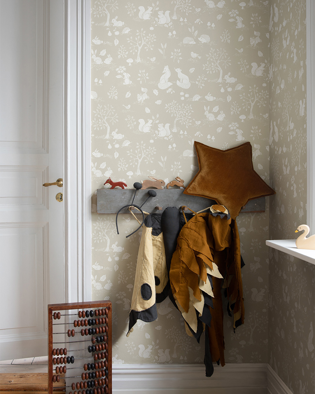 Beige children's wallpaper featuring animals and trees in a cute children's room with a hook rail and clothes and toys hanging from it