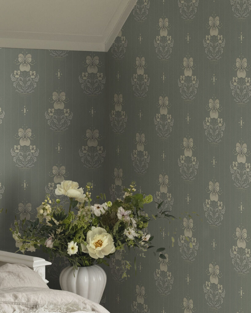 Grågrön tapet bakom en vit vas med blommor i ett sovrum