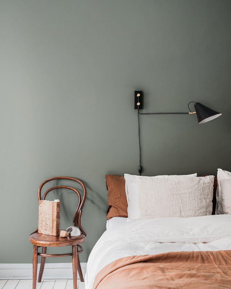 Gray-green solid-color wallpaper in a bedroom with a made bed featuring orange bedding