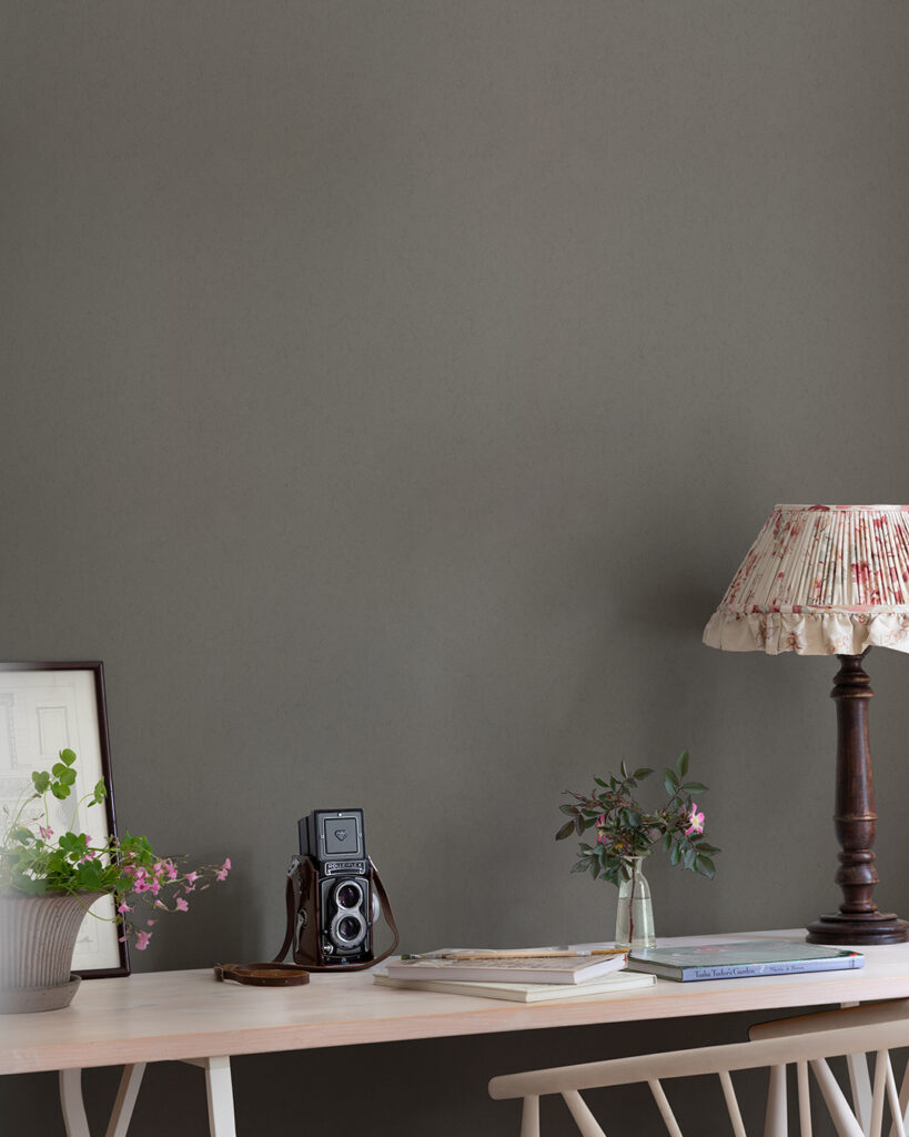 Dark brown wallpaper behind a table with books and a lamp on a wooden table