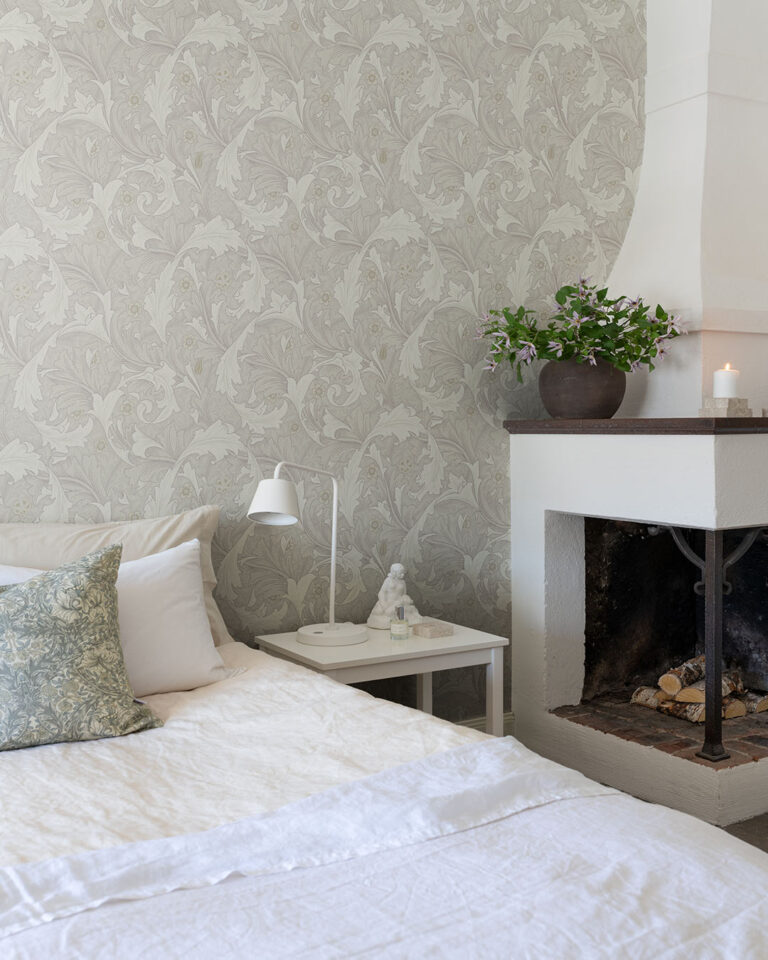 Gray-beige William Morris wallpaper with white leaves behind a white bed and a fireplace