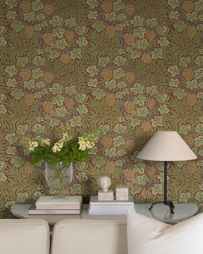 Wallpaper with a burgundy background and green leaves in front of a vase of flowers and a table lamp