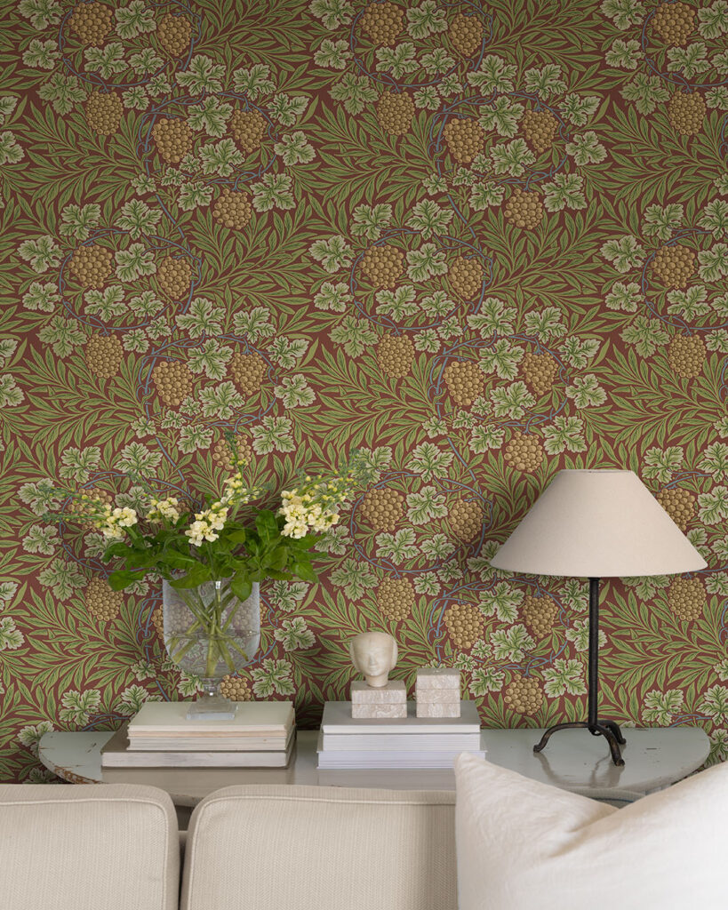 Wallpaper with a burgundy background and green leaves in front of a vase of flowers and a table lamp