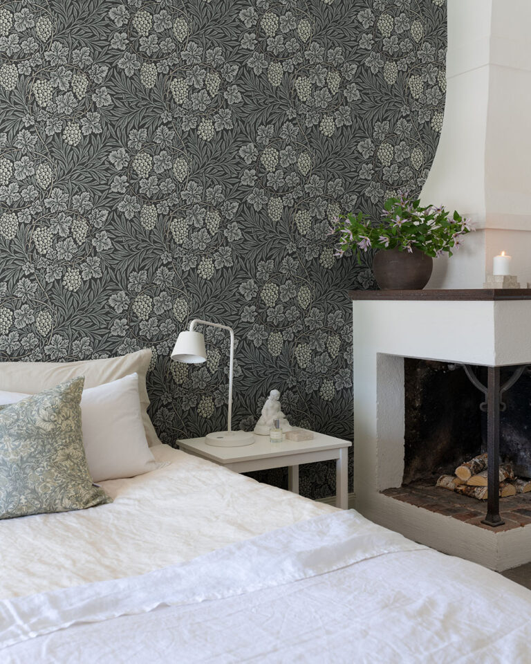 Wallpaper with a black background and gray leaves in a bedroom behind a bed and a fireplace