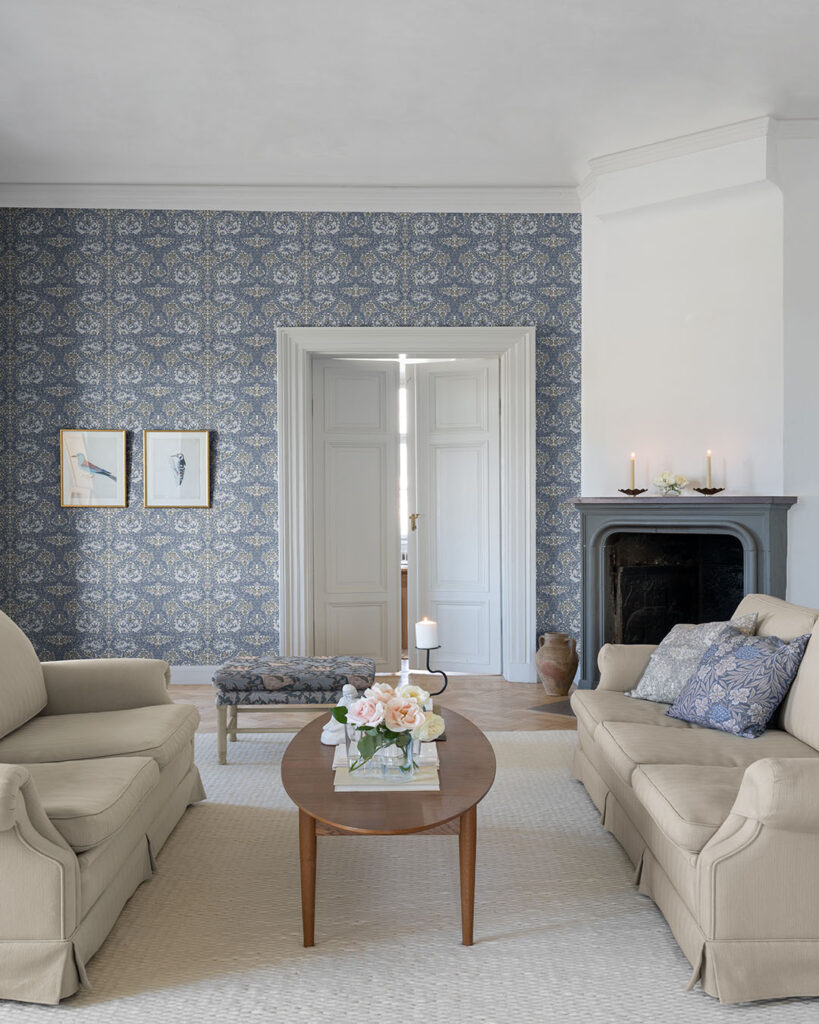 A vibrant wallpaper with blue leaves and a white background in a large living room with two sofas and a coffee table