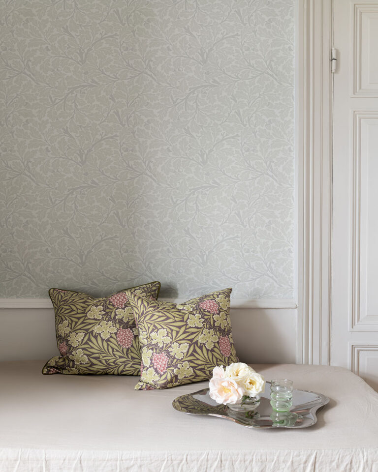 Light gray wallpaper featuring oak leaves behind two decorative pillows adorned with leaves and grapes