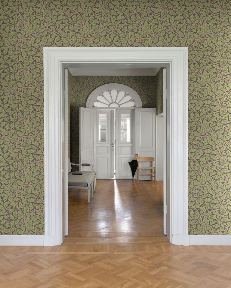 Wallpaper with a plum-purple background and green oak leaves in an open hallway with white door trim