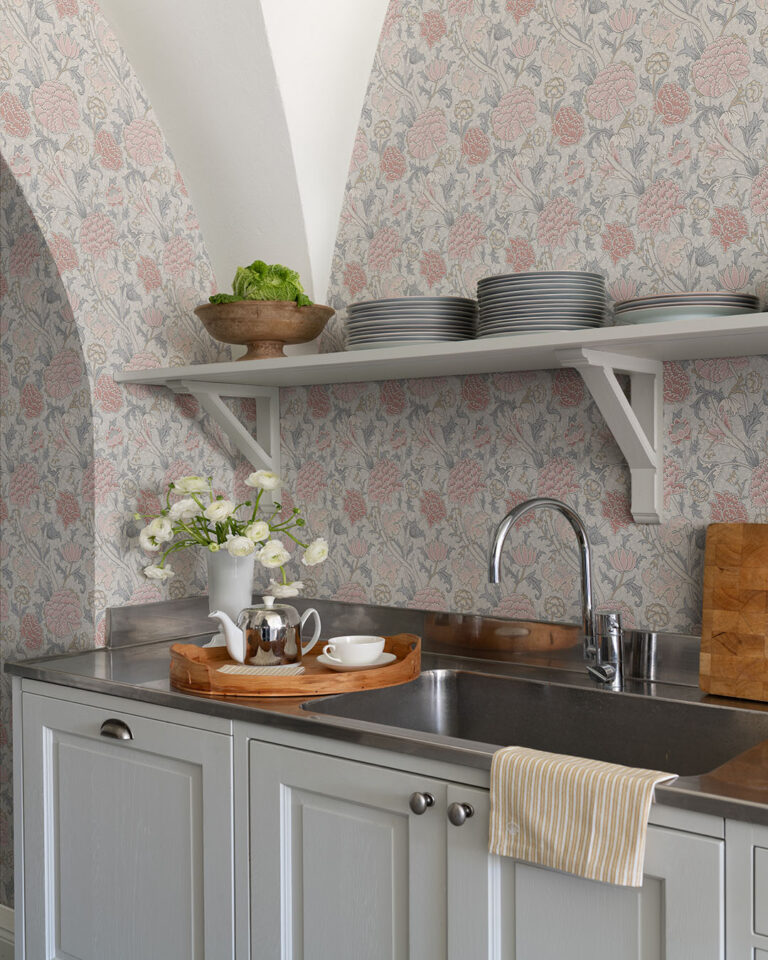 Pink floral wallpaper by William Morris in a kitchen behind a sink with a wooden tray and a bouquet of white flowers