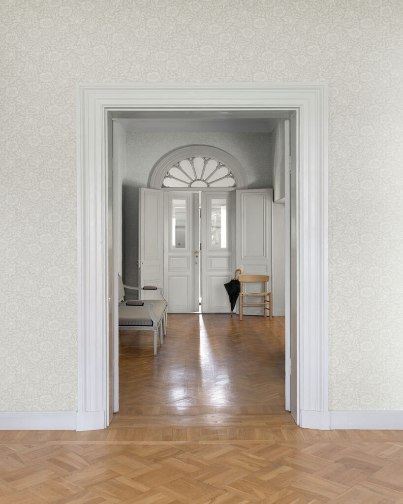 Light gray wallpaper in an open hallway with white doors and baseboards