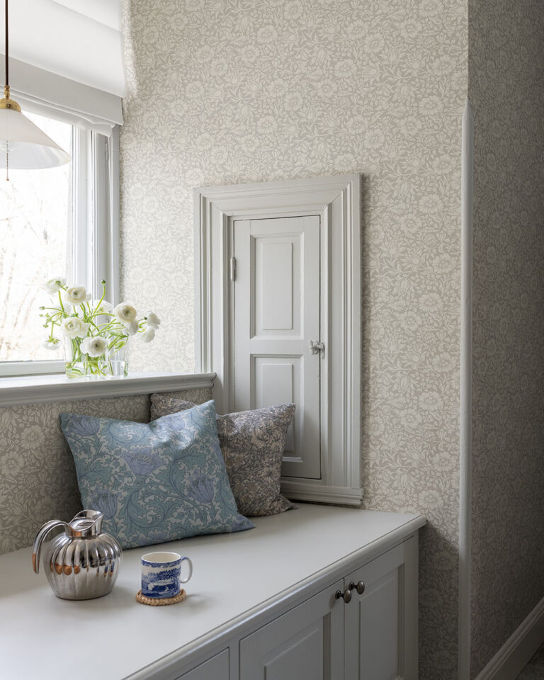 A corner with a built-in bench by a small window, featuring beige floral tone-on-tone wallpaper.
