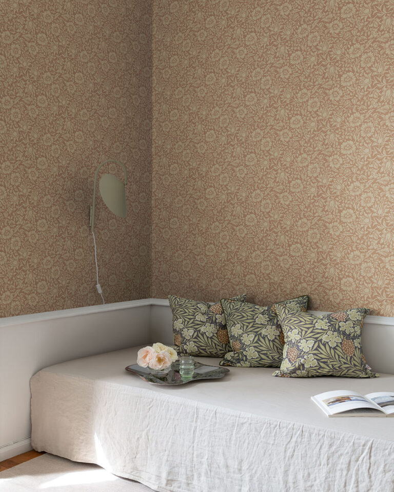 Terracotta wallpaper with flowers and leaves behind a sofa with pillows