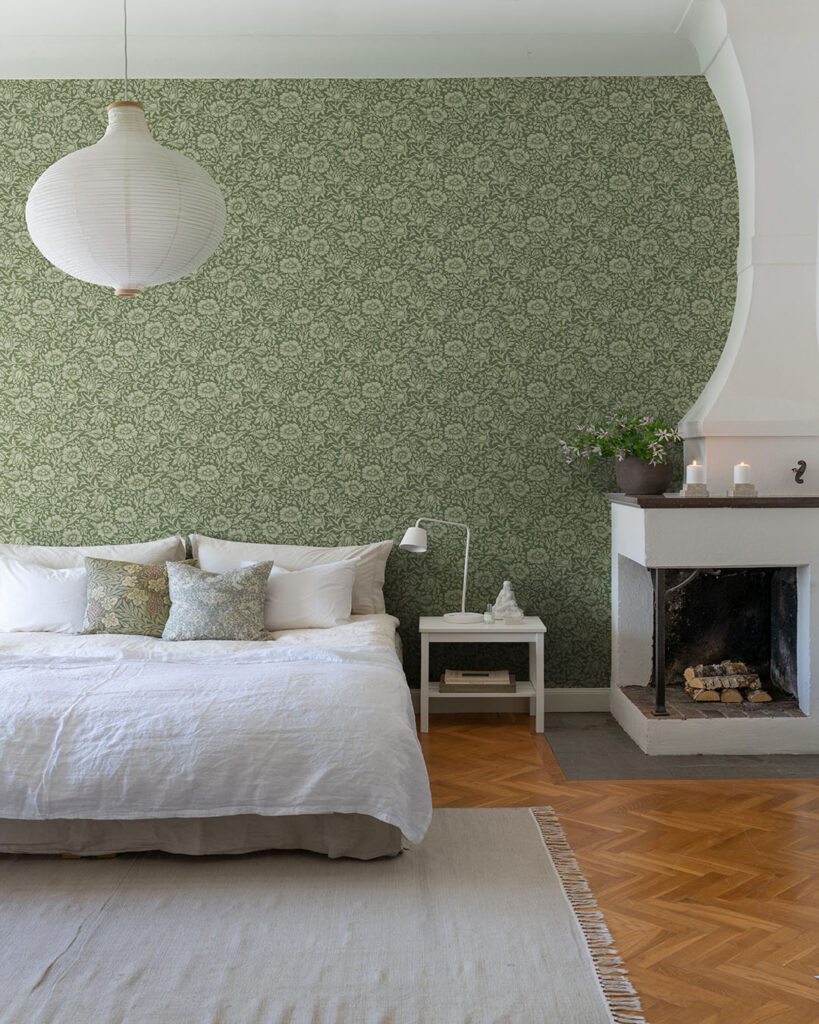 Grön och blommig William Morris tapet i ett sovrum bakom en stor bäddad säng