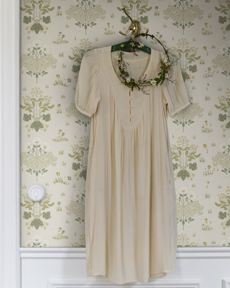 Light-colored floral wallpaper behind a dress hanging on a hook