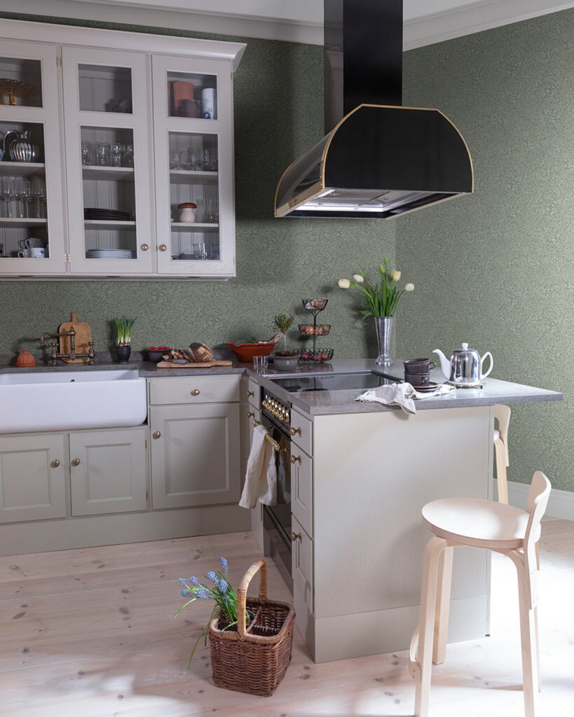 A kitchen with gray cabinetry and a black range hood, featuring tone-on-tone green wallpaper.