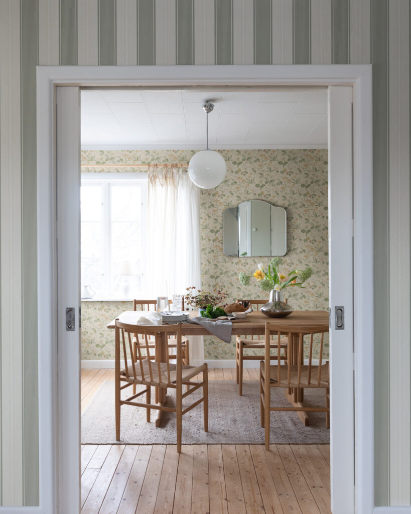 Yellow wallpaper with flowers in a large dining room with a wooden table and chairs