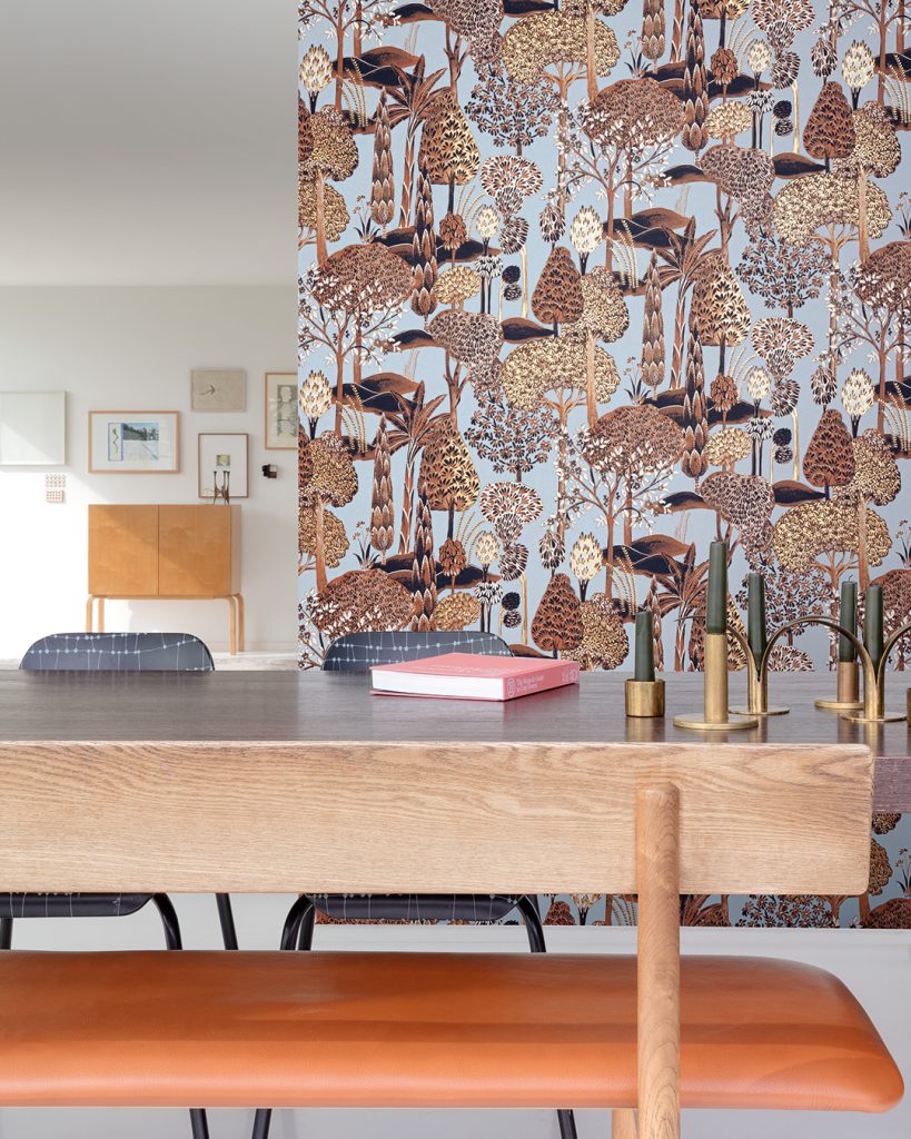Wallpaper with a light blue background and brown trees in a dining room with a large wooden table