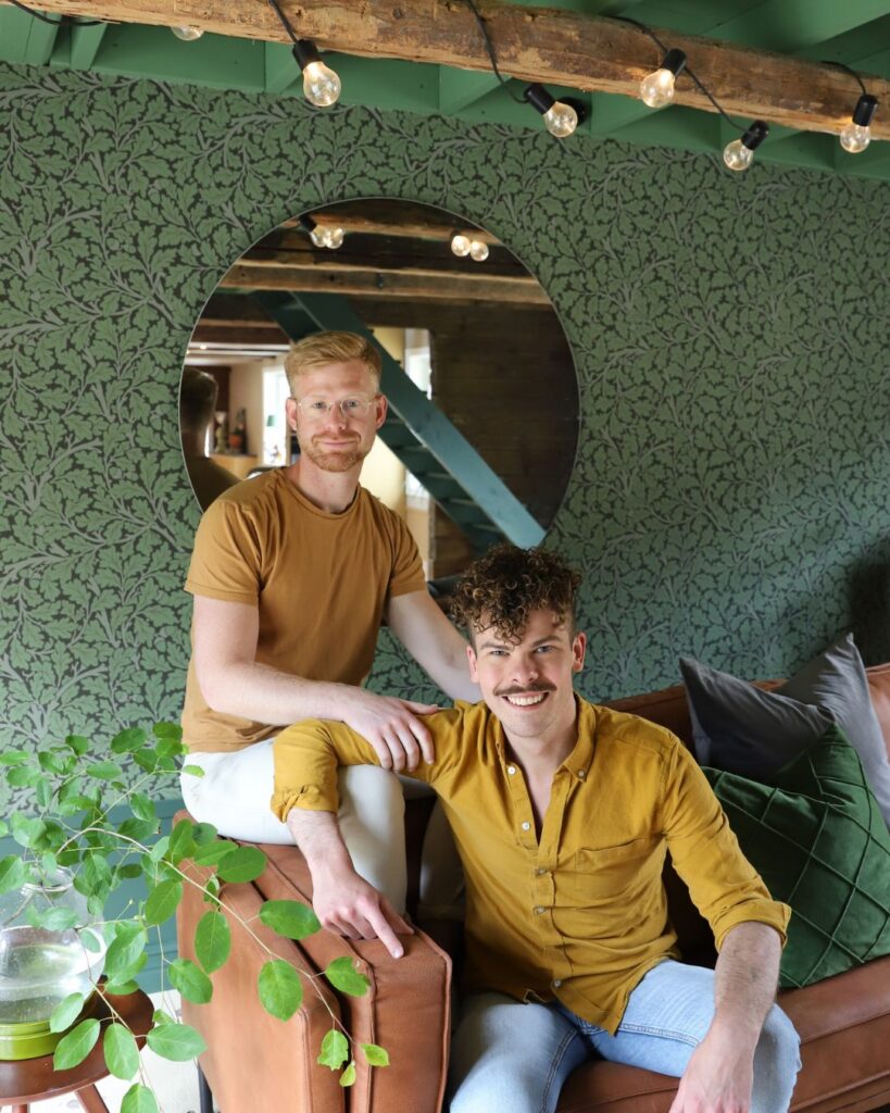 Simon och anders sitter i soffa framför bladmönstrad tapet